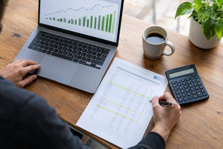Empreendedor analisando o fluxo de caixa da agência no notebook, com extrato bancário e calculadora
